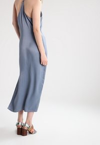 Vestido maxi en satén azul claro, con un diseño de espalda drapeada. Combinado con sandalias de tacón alto en múltiples colores y un tacón de bloque de madera.
