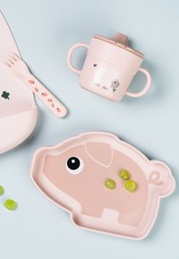 Roze plastic bord in de vorm van een varken met groen voedsel, roze beker met schapenontwerp en een vork met bloemenaccenten op het handvat.