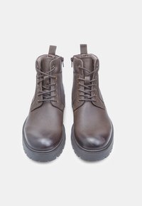 Stivali ankle in pelle marrone con finitura testurizzata, punta rotonda e occhielli metallici. Presentano lacci e zip laterale per una facile calzata.