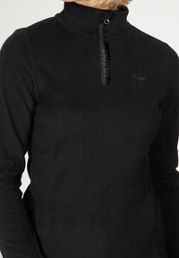 Sudadera de forro polar negra con cuello alto, que incluye una cremallera de media longitud y un logo bordado. Textura suave, diseño minimalista.