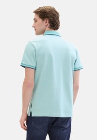 Lichtblauwe polo shirt met een zachte textuur, voorzien van donkerblauwe accenten op de kraag en mouwen. Zijsplitten aan de onderkant.