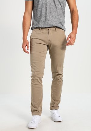 Beige chinos se slim fit, vyrobené z bavlněné směsi. Mají zipový zavírání, přední kapsy a hladkou texturu. Kombinované s šedým tričkem.