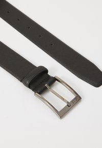 Fekete bő öv texturált felülettel, ezüst fém csat és több lyuk a méretállításhoz. A pánton látható a "BOSS" márkájú felirat.