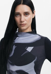 Cămașă cu mânecă lungă și guler înalt, cu un model abstract în nuanțe de negru și gri. Fabricată dintr-un material neted și elastic, cu un design ajustat.