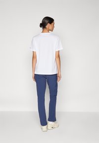 White short-sleeve t-shirt paired with blue trousers. The t-shirt features a round neckline and relaxed fit, while trousers have a smooth texture.