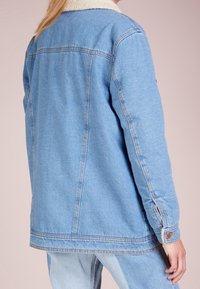Jeansjacka i ljusblått med en krämfärgad fake shearling-krage, långa ärmar och knäppte manschetter. Har en avslappnad passform och ryggsömmar.
