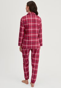 Rotkariert Pyjama aus Flanell mit langen Ärmeln und elastischen Bündchen an den Hosen. Die Rückansicht zeigt eine lockere Passform und einen geknöpften Kragen.