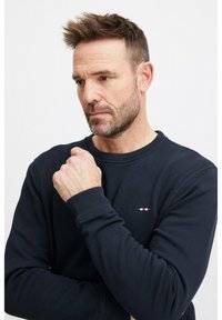 Felpa blu navy con scollo rotondo, polsini a coste e un piccolo logo ricamato. Tessuto morbido e vestibilità comoda.