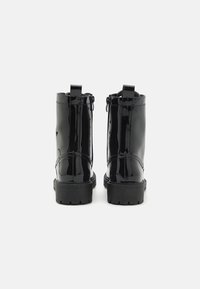 Czarne botki z lakierowanej skóry z masywną czarną podeszwą, gładką fakturą, zamkami błyskawicznymi z tyłu oraz pętelkami na pięcie ułatwiającymi zakładanie.