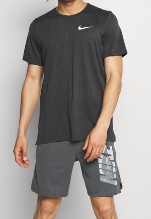 Nike Sportoutfit bestehend aus einem schwarzen, kurzärmeligen T-Shirt mit strukturiertem Muster, kombiniert mit grauen Shorts, die auffällige weiße Grafiken zeigen.