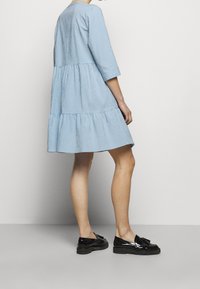 Blå rutmönstrad klänning med trekvartslång ärm, lagd fåll och en lös passform, i kombination med svarta blanka loafers. Slät tygkvalitet.