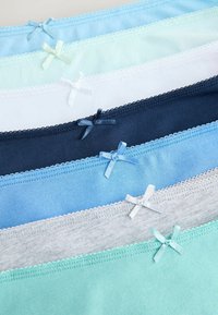 Pile de sept sous-vêtements féminins dans des couleurs pastel et neutres, chacun orné d'un petit nœud assorti au centre de la ceinture.