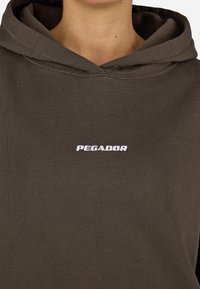 Brązowy kaptur z nadrukiem "PEGADOR" w białym kolorze. Wykonany z miękkiego materiału, o prostym, minimalistycznym wzorze.