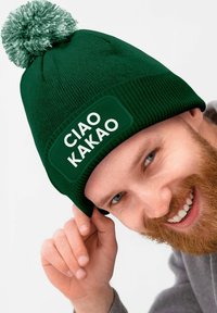 Green knitted beanie with a textured finish, featuring a white patch with "CIAO KAKAO" text and a green pom-pom on top.