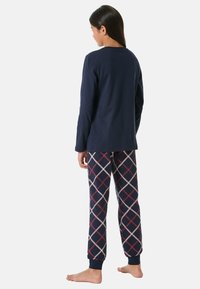 Marinblå tröja med långa ärmar som matchas med mönstrade pyjamasbyxor med diamantdesign i marinblått, röd och krämfärgad. Mjuk bomullsmaterial.
