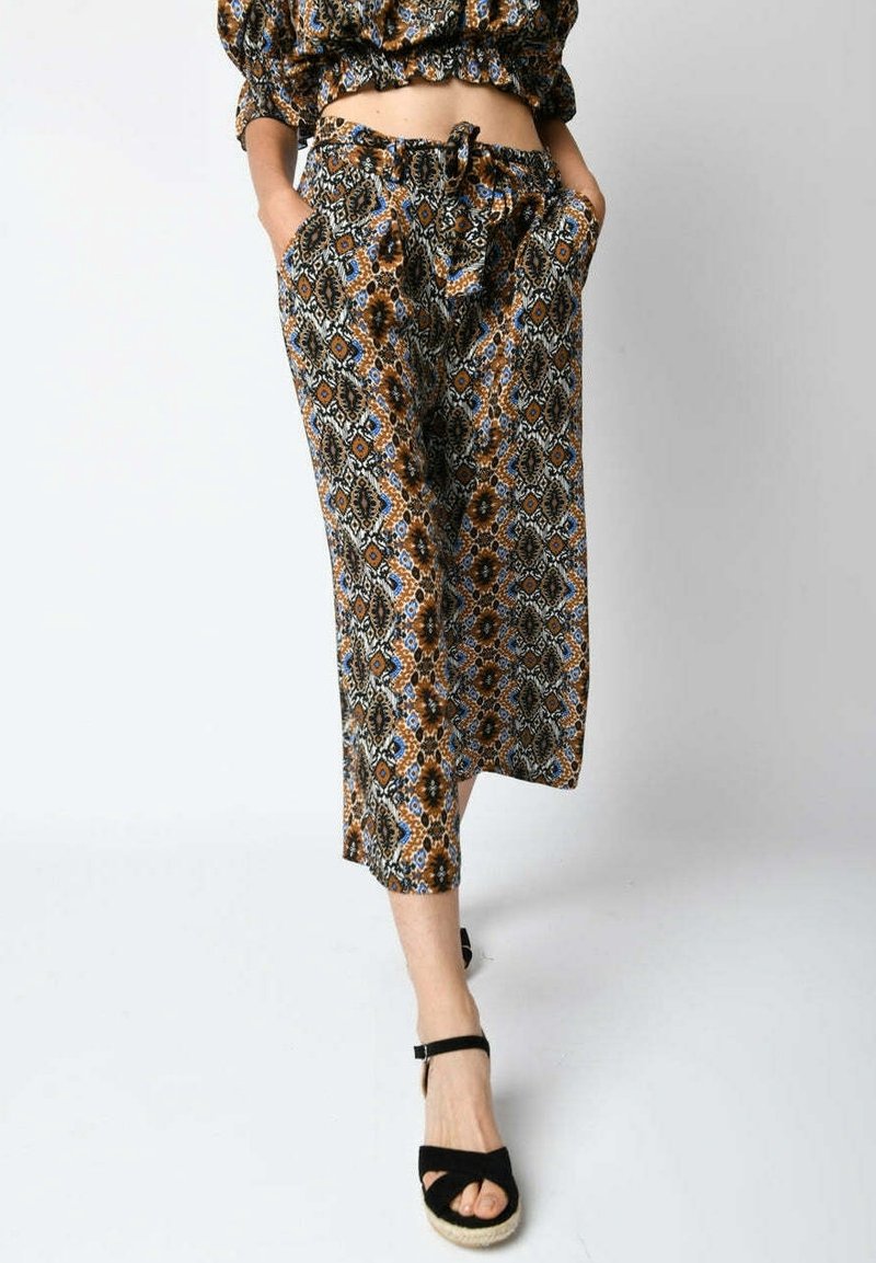 Femme portant un pantalon court à jambes larges avec un motif géométrique marron, bleu et noir et des sandales compensées noires à bride cheville.