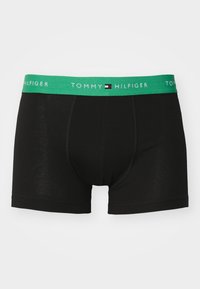 Boxer noir avec une ceinture élastique verte portant le nom de la marque "TOMMY HILFIGER" et son logo. Tissu doux avec une coupe ajustée.