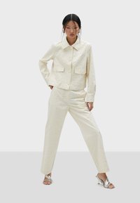 Witte jas en broek set met stippenversieringen, met een kraag, twee voorzakken en zilveren hakken. Glad stoftextuur.