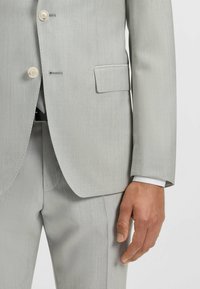 Jasnoszary garnitur z dopasowaną marynarką z pojedynczym zapięciem, dwoma guzikami i klapami w kształcie litery notch. Gładka tkanina i spodnie w wąskim kroju.