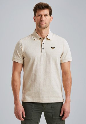 Polo beige avec un motif texturé, patte de boutonnage à trois boutons, et un petit logo noir et or sur la poitrine gauche. Manches courtes.