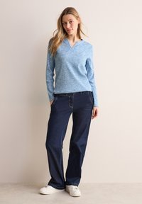 Svetle modrá košile s dlouhým rukávem a henley límcem, doplněná tmavě modrými rovnými džíny. Celý outfit dotváří bílé tenisky.