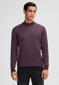 Lila langärmliger Rollkragenpullover aus weichem Material mit geripptem Kragen und Ärmeln, kombiniert mit schwarzen Jeans.