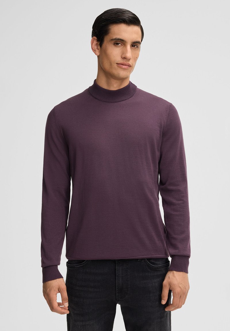 Lila langärmliger Rollkragenpullover aus weichem Material mit geripptem Kragen und Ärmeln, kombiniert mit schwarzen Jeans.