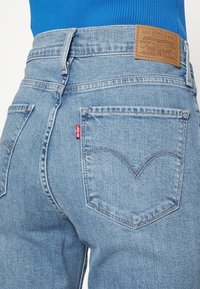 Ljusblå denimjeans med hög midja, med en läderlapp med texten "Levi Strauss & Co." och en liten röd tagg på bakfickan.