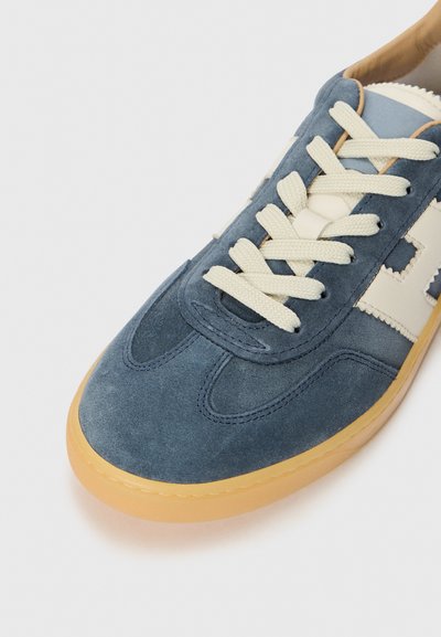 Sensuede sneakers i mørkeblå med elfenbensfargede snører, med en kontrasterende elfenbensfarget logo detalj og en beige gummisåle, glatt tekstur.