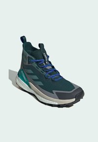 Grüner und grauer Sportschuh mit einer hohen Schnittführung, strukturiertem Stoff, gepolstertem Schaft, blauen Schnürsenkeln und einer weißen Zwischensohle mit schwarzem Rutschfester Sohle.