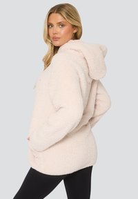 Lichtroze fleece hoodie met een gezellige textuur, grote capuchon, voorzakken en een losse pasvorm, gecombineerd met zwarte legging.