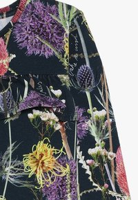 Tmavá tkanina s květinovým vzorem, obsahující fialové, žluté a bílé květiny. Zahrnuje nařasený akcent na výstřihu.