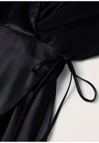 Tissu de robe portefeuille noire à texture fine noué avec un ruban étroit en satin en forme de nœud sur une surface blanche.