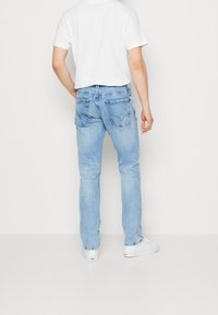 Lichtblauwe denim jeans met een rechte snit, voorzien van twee achterzakken en een vervaagde afwerking. Gepaard met een wit t-shirt met korte mouwen.