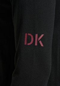 Svart idrottstopp med ett mönster av texturerad mesh och en framträdande maroon "DK"-logotyp på ärmen.