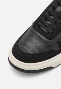 Svart sneakers med en kombination av perforerat läder och mocka. Tjock vit mellansula och strukturerad svart sula. Snördesign med platta snören.