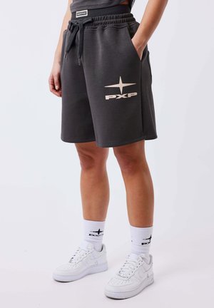 Persoon die donkergrijze PXP-shorts met trekkoord draagt, witte sokken met zwart ontwerp en witte sneakers, staand tegen een effen lichte achtergrond.