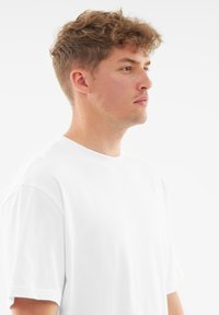 Biała bawełniana koszulka z okrągłym dekoltem i krótkimi rękawami, o luźnym kroju i dyskretnym logo na piersi.