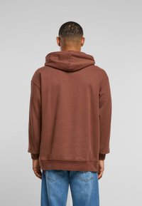 Brun hettegenser med lange ermer, avslappet passform og ribbede mansjetter, kombinert med lyseblå jeans. Glatt, teksturert stoff.