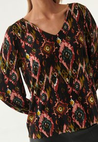 Haut à manches longues en V avec un motif géométrique multicolore sur fond noir, fabriqué en tissu doux avec une coupe légèrement ample.