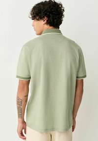 Polo cu manecă scurtă, de culoare verde deschis, cu un design texturat și modelat. Prezintă guler și mansete asortate cu detalii contrastante.