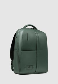 Mochila de cuero verde con diseño estructurado, asa superior, superficies lisas y bolsillo delantero. Cierre con cremallera y detalle de logo en relieve.