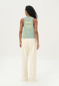Mintgroene mouwloze top met tekst op de rug, gecombineerd met crèmekleurige wijde broek. Soepele textuur, minimalistisch ontwerp en casual pasvorm.
