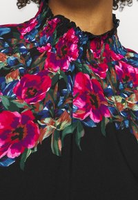 Blouse en tissu noir avec un col froncé, ornée de motifs floraux vibrants en rose et bleu et d'une finition texturée.