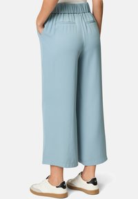Pantaloni larghi di colore azzurro chiaro con vita elastica, dotati di due tasche laterali e una superficie liscia. Abbinati a sneakers bianche.