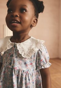 Kleid mit Blumenmuster, kurzen Puffärmeln, weißem Lochstickkragen und Knöpfen in Pastellfarben vor hellem Hintergrund.