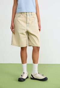 Ljusbeiga denimshorts med en avslappnad passform, femficksdesign och lätt blekning. Matchas med beige och svarta skor samt vita strumpor.