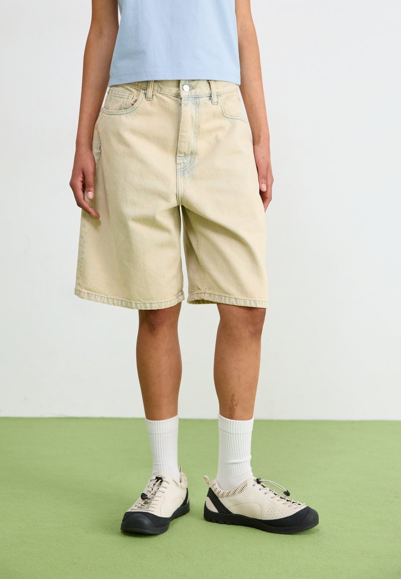 Ljusbeiga denimshorts med en avslappnad passform, femficksdesign och lätt blekning. Matchas med beige och svarta skor samt vita strumpor.