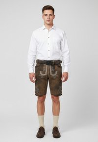 Ruokohjeet: ruskeat nahka lederhosenit, joissa on koristeellinen brodeeraus, yhdistetty valkoiseen napitettavaan paitaan ja polvipitkiin beigeihin sukkiin, viimeistelty tummilla kengillä.