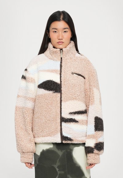 Veste en polaire avec fermeture éclair, présentant un mélange de motifs beige, marron, noir et bleu clair. Texture douce et col haut.